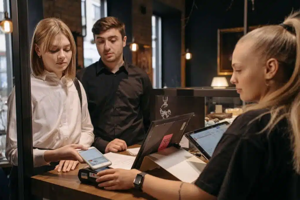 Customer service representative helping young customer set up a Venmo teen account using mobile payment system at a retail counter, with digital tablets and payment terminal visible.